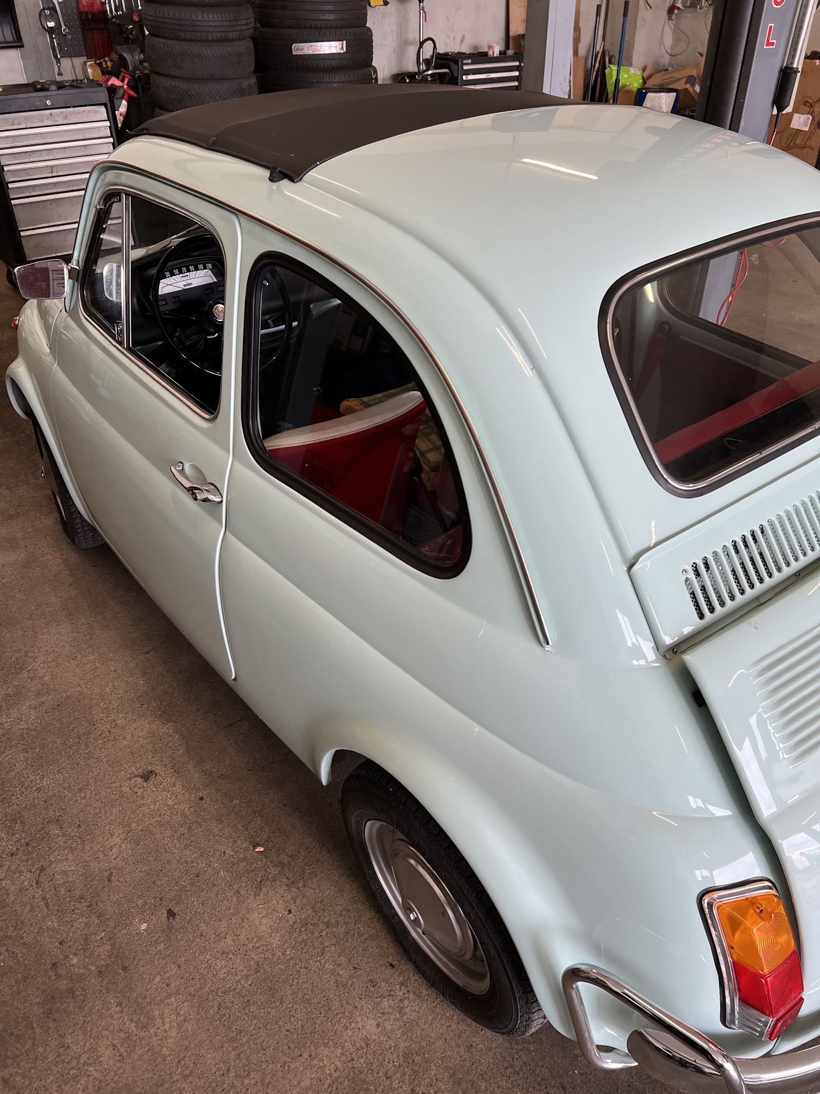 Mintgrüner Fiat 500 in der Werkstatthalle, dahinter Reifenstapel und Werkzeugwagen